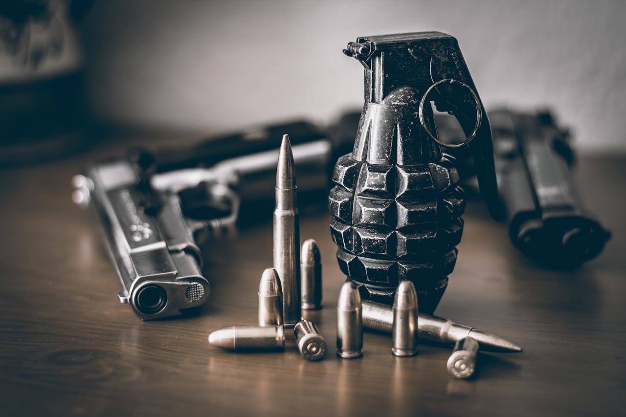 A collection of weapons including a pistol, grenade, and bullets on a wooden surface.