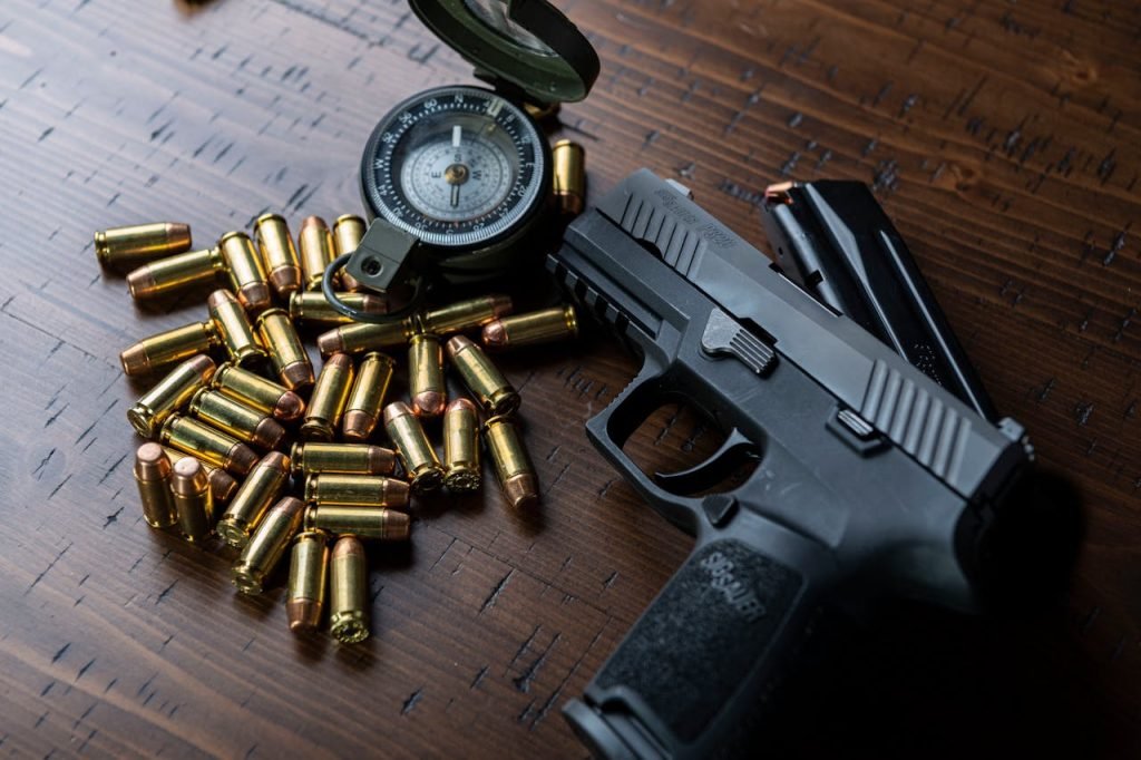 High-angle shot of a handgun, bullets, and a compass resting on a wooden surface.