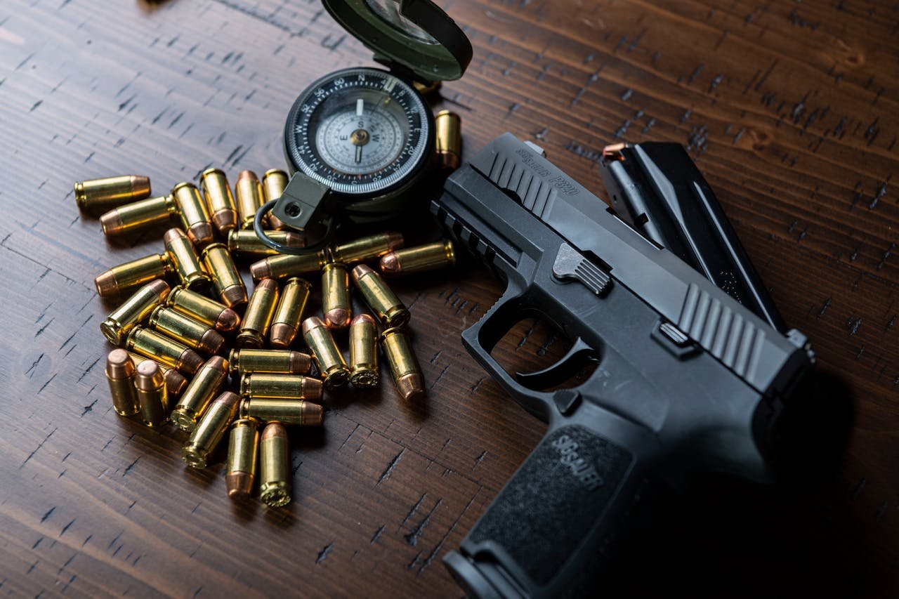 High-angle shot of a handgun, bullets, and a compass resting on a wooden surface.