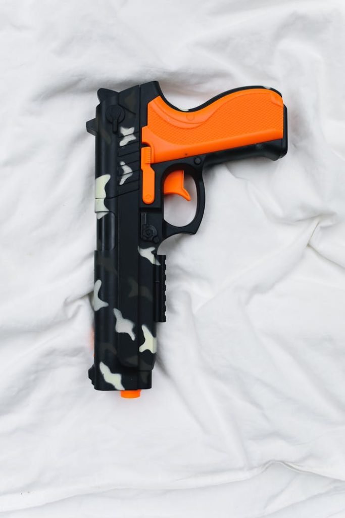 Plastic toy gun with orange accents and camouflage pattern on white fabric.